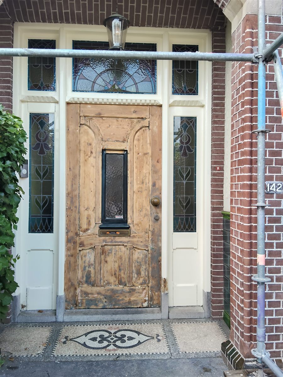 Verweerde houten voordeur met glas-in-lood voor behandeling